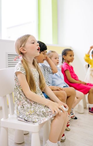 Four children sitting in chairs singing.