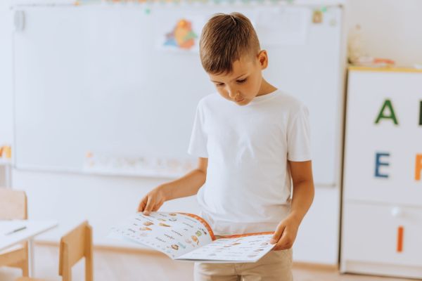 Young boy standing at the front of the classroom reading.